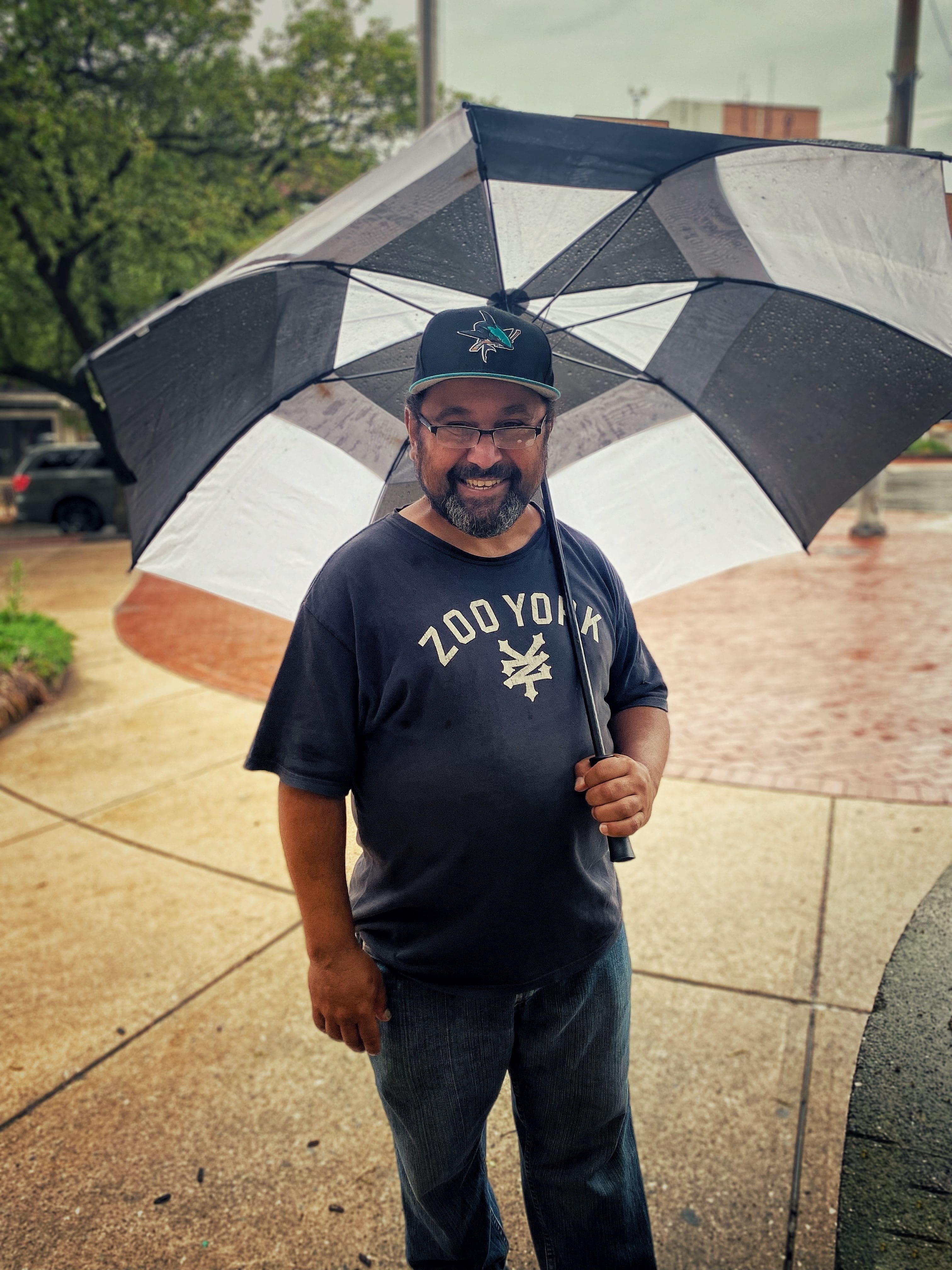 Man in a Zoo York T-shirt smiling and holding a big black and white umbrella.